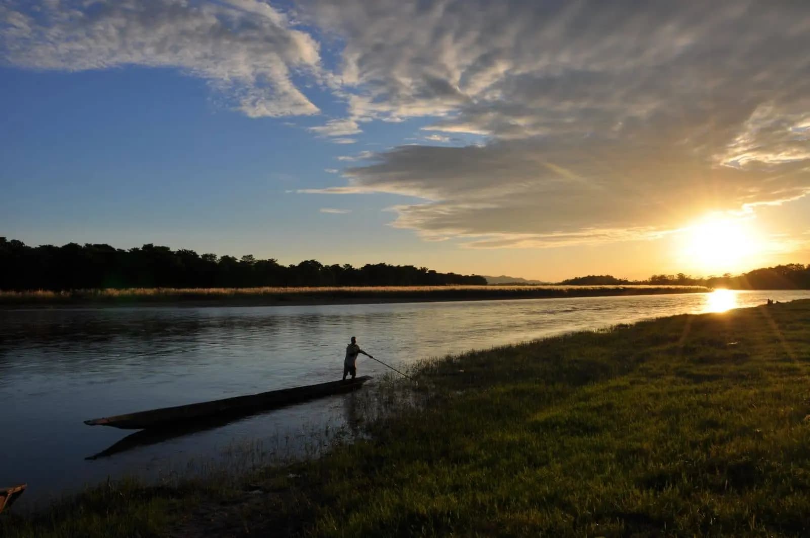 un conducteur de pirogue népalais s'éloigne de la berge avec un magnifique coucher de soleil